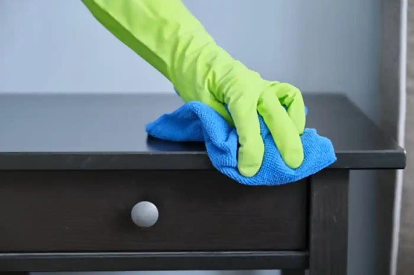 Gloved hand wiping down a dark wood dresser during a detailed deep cleaning