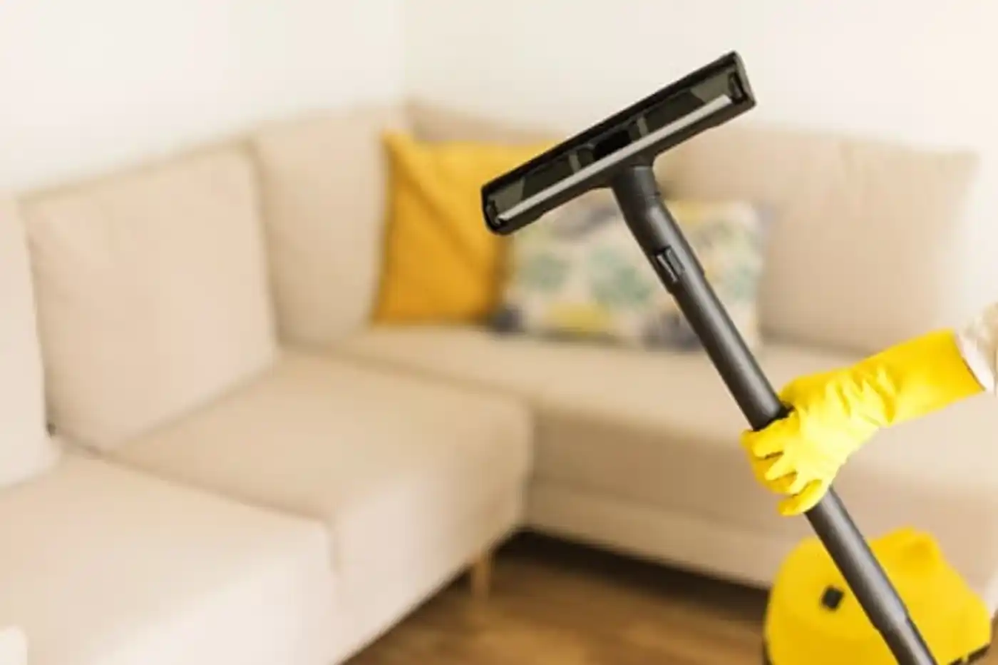 Vacuuming beneath a grey sectional sofa during a standard house cleaning